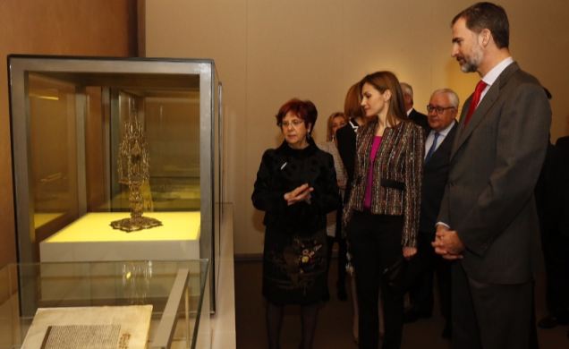 Sus Majestades los Reyes atienden las explicaciones de la comisaria de la exposición, Carmen Morte